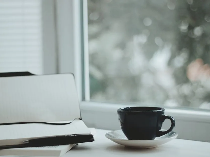 Une tasse et un carnet ouvert près d’une fenêtre
